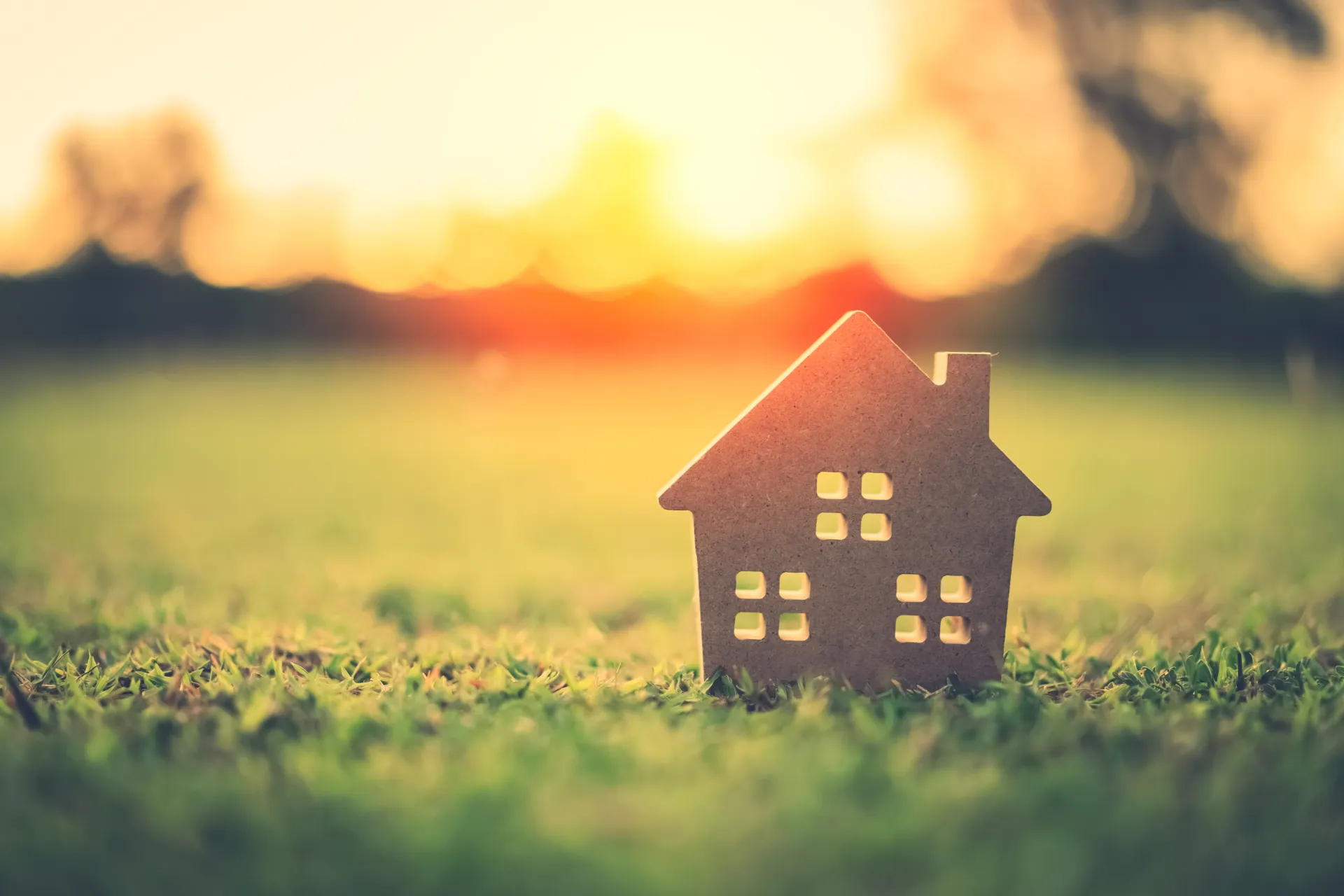 Small wooden house model on grass at golden sunset
